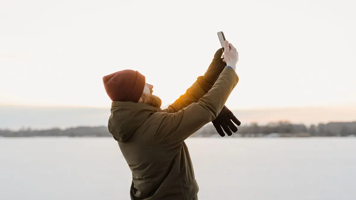 A person in a winter coat holding up a phone on a frozen lake at sunset near Edmonton, reading a loan offer and its instalment dates before signing